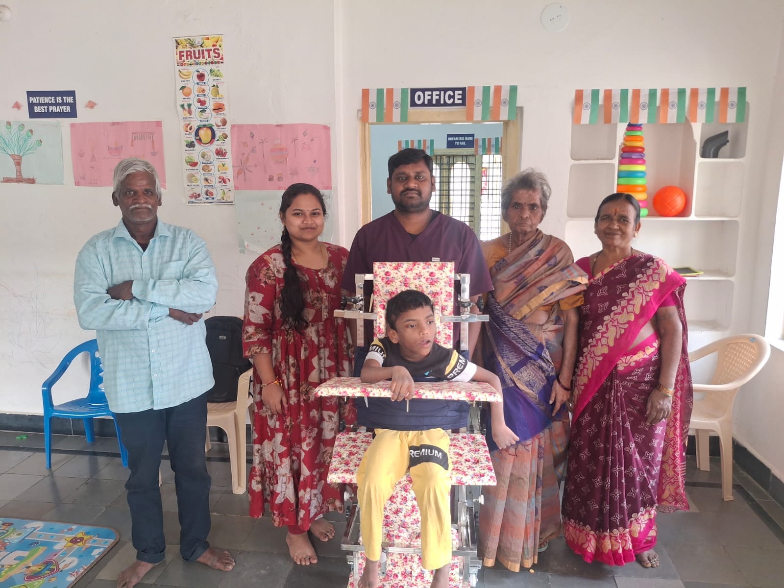 Family with a child in an assistive standing frame, with trustees and staff at the special school